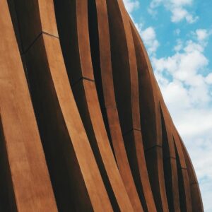 Vertical shot of a contemporary wavy concrete facade against a cloudy blue sky, showcasing modern design.