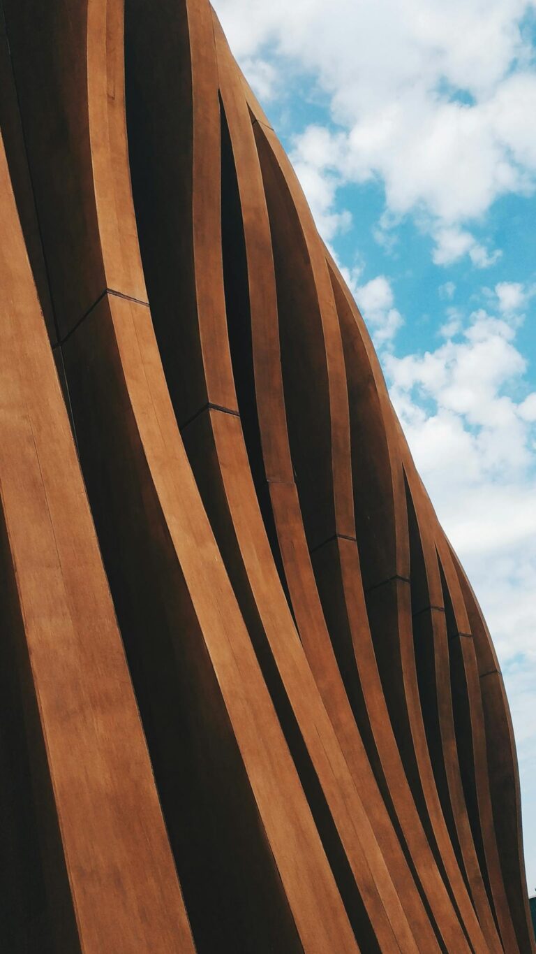 Vertical shot of a contemporary wavy concrete facade against a cloudy blue sky, showcasing modern design.